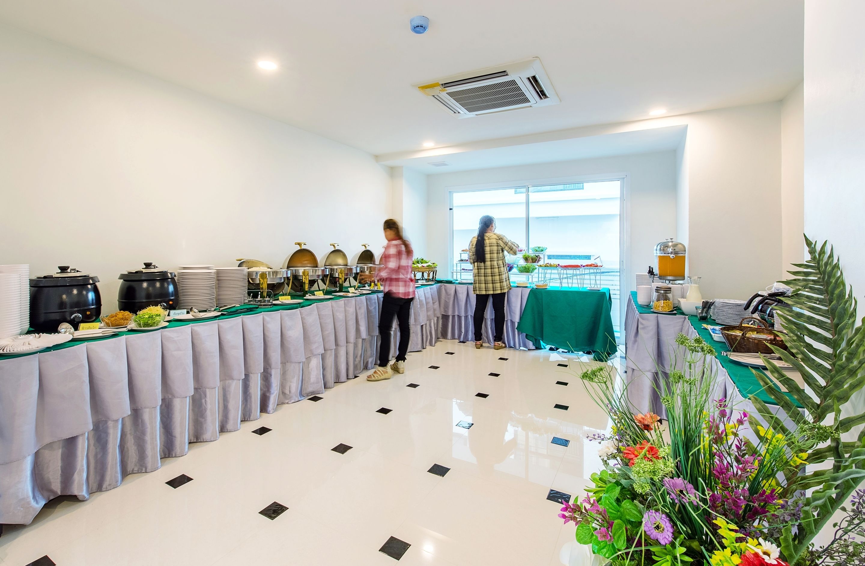 Un buffet avec plusieurs présentoirs de nourriture, une table verte avec un téléphone et un panier, et une grande fenêtre en arrière-plan.