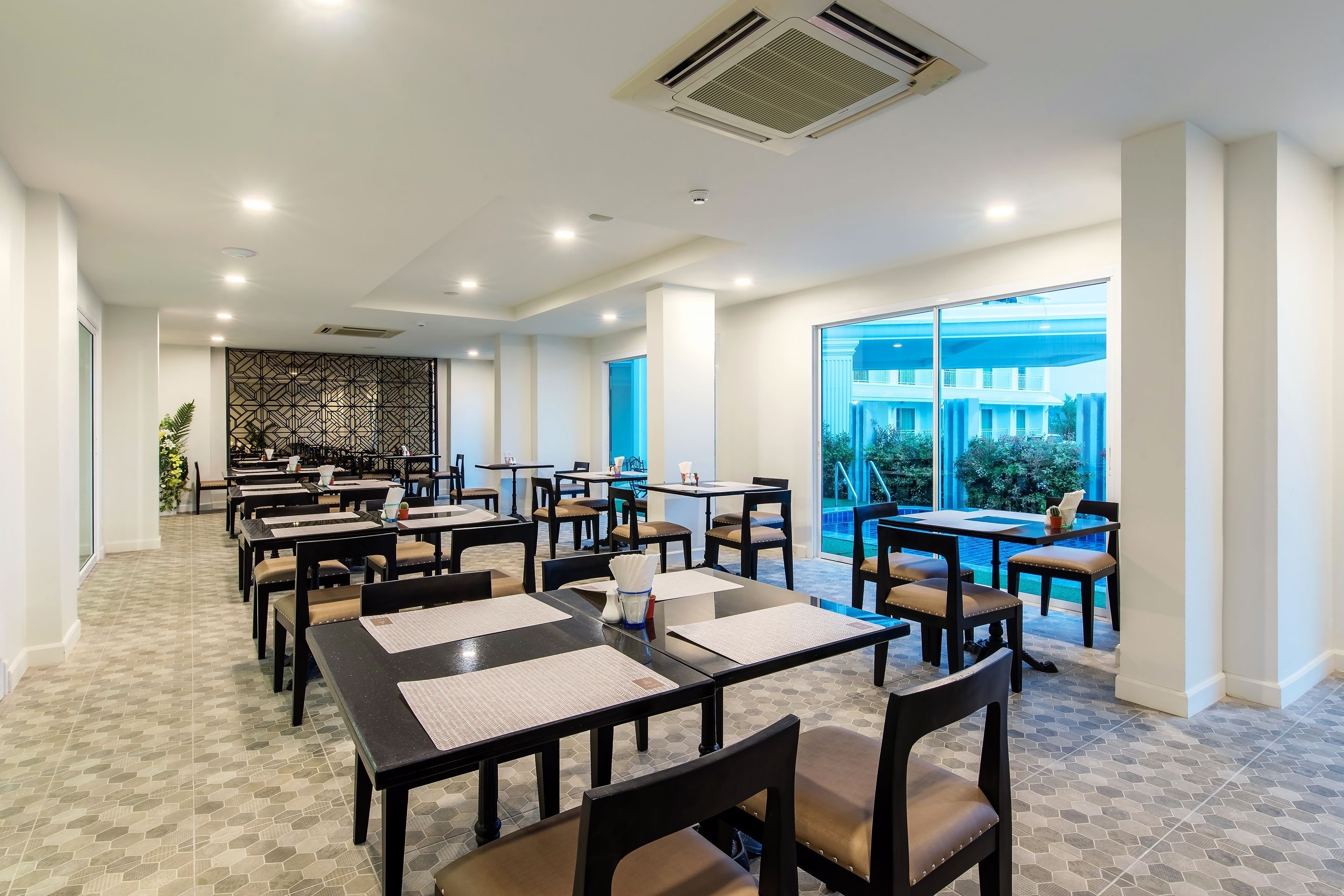 Un amplio comedor interior con varias mesas y sillas, ventanas grandes que ofrecen vistas al exterior, y una pared decorativa al fondo.