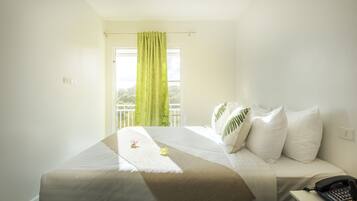 A neatly made bed with a white and beige bedspread, a green curtain, and a telephone on a bedside table.