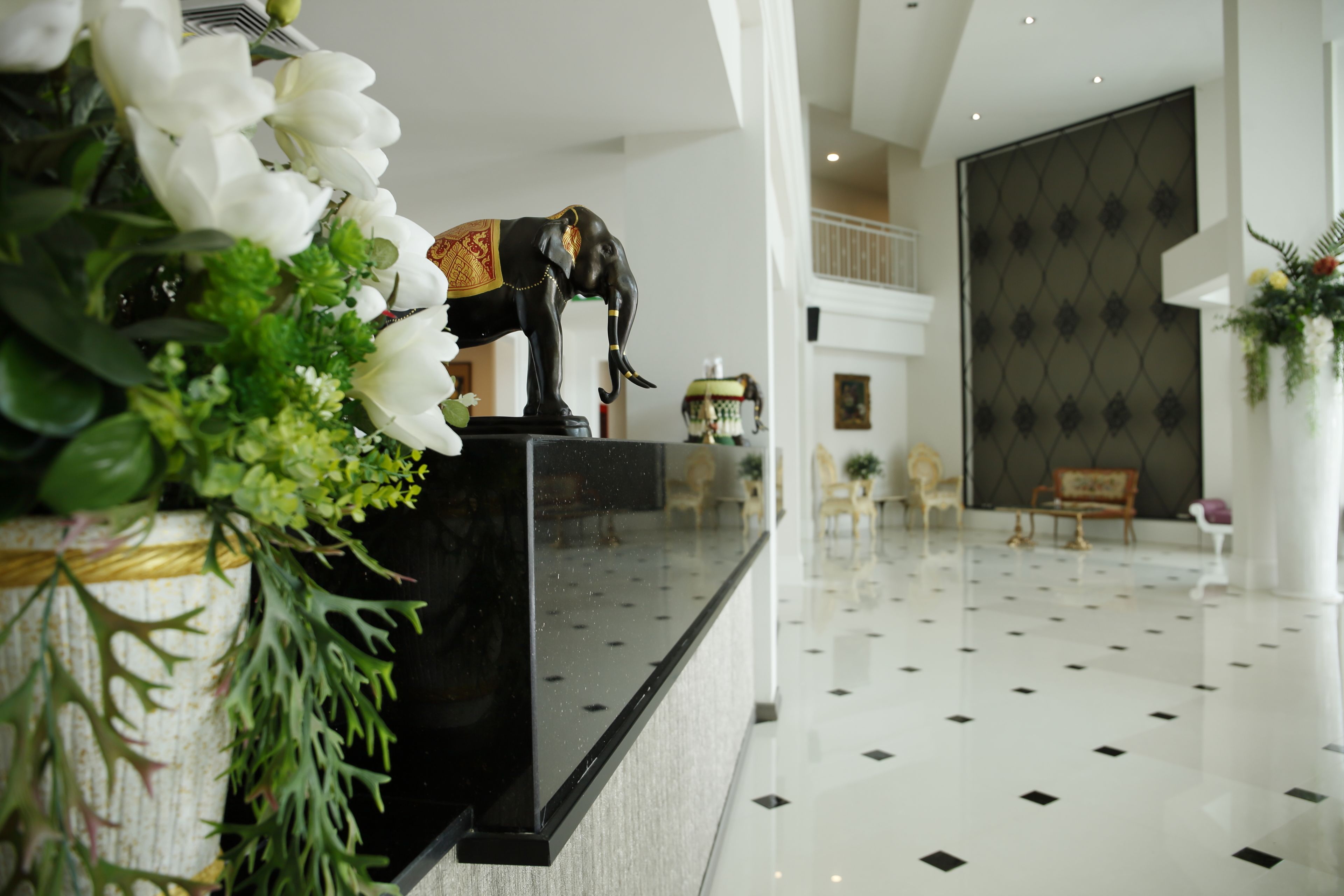 Un espace d’accueil avec un comptoir noir, une statue d’éléphant décorative et un arrangement floral.