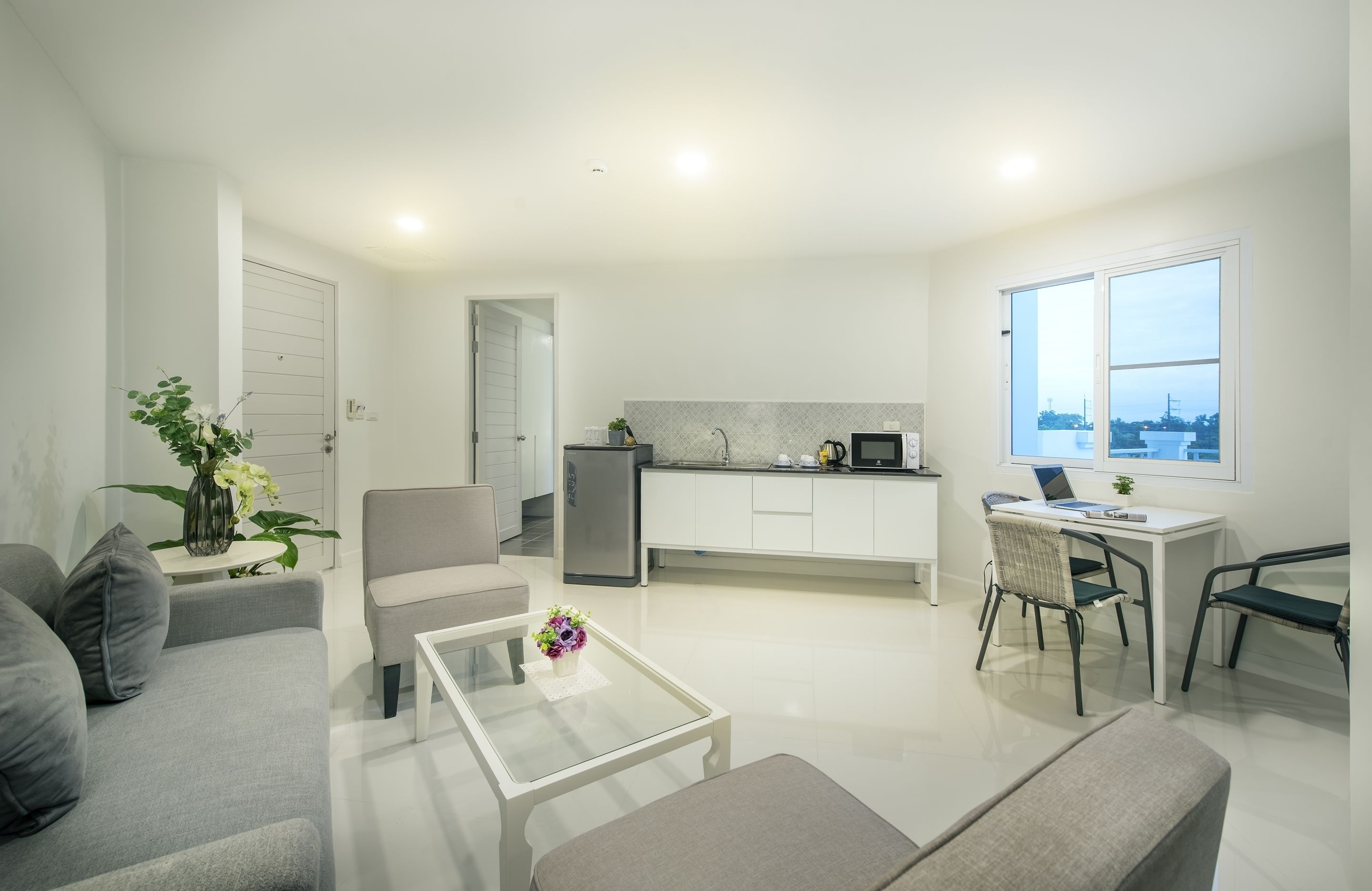 Una sala de estar moderna con sofá, mesa de centro y sillas, una cocina con refrigerador y microondas, y un ventanal con vistas.