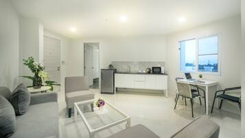 Una sala de estar moderna con sofá, mesa de centro y sillas, una cocina con refrigerador y microondas, y un ventanal con vistas.