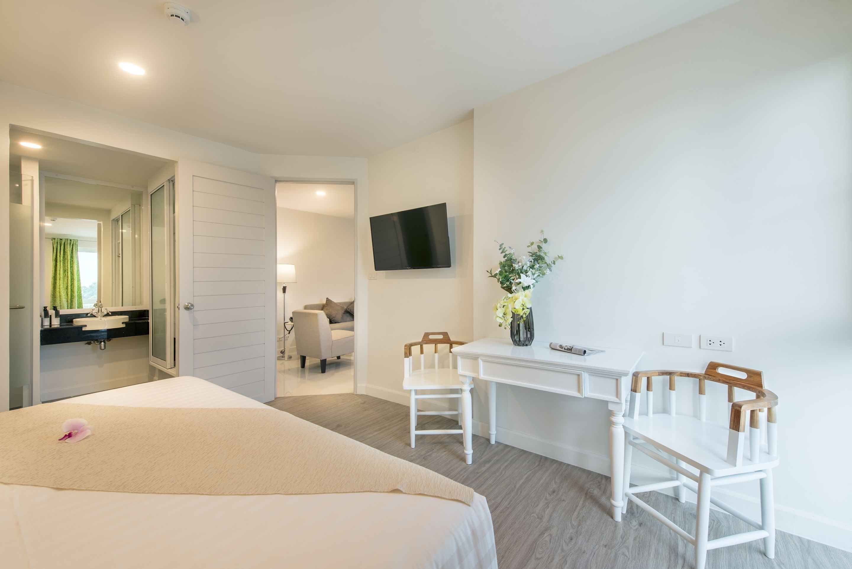 A hotel room with a bed, a desk, two chairs, a TV, and a bathroom visible through an open door.