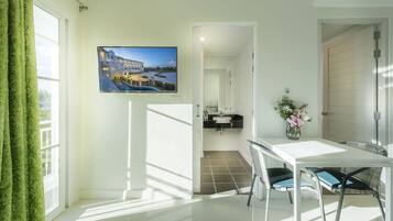 A bright room with a TV displaying a resort, a white table with chairs, and a view of a pool through the window.