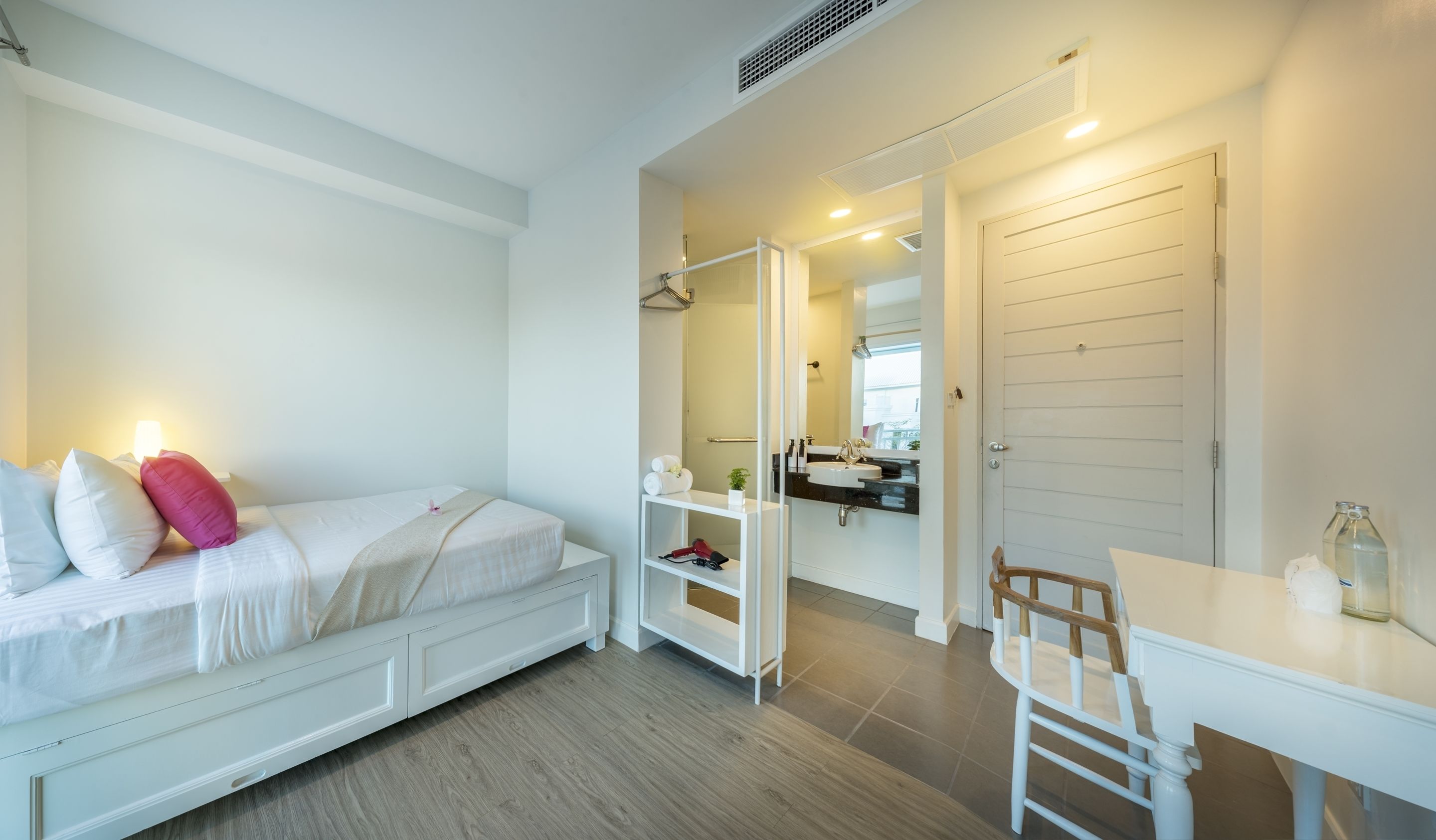 Un dormitorio con cama, mesita de noche y un pequeño escritorio con silla. Hay un espejo y una puerta que da al baño.