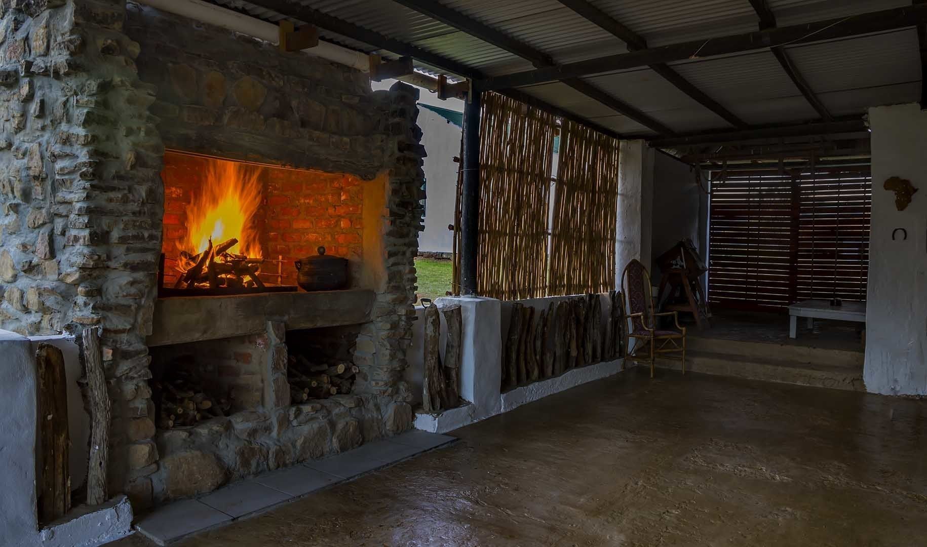A stone fireplace with a fire, a bamboo wall, and a metal roof in a rustic interior.