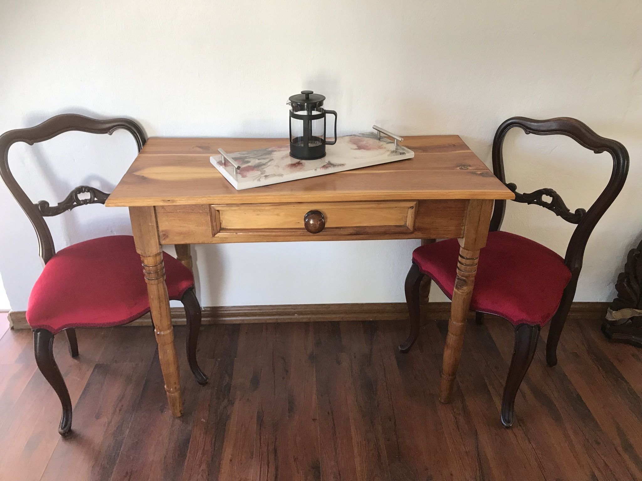 A wooden table with a drawer, two red upholstered chairs, and a decorative item on the table.