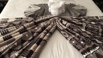 A neatly made bed with a patterned blanket, a zebra-themed pillow, and rolled towels.
