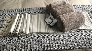Een bed met een metalen hoofdbord, een kussen met een neushoornprint en een opgevouwen handdoek op een kamerbreed tapijt.