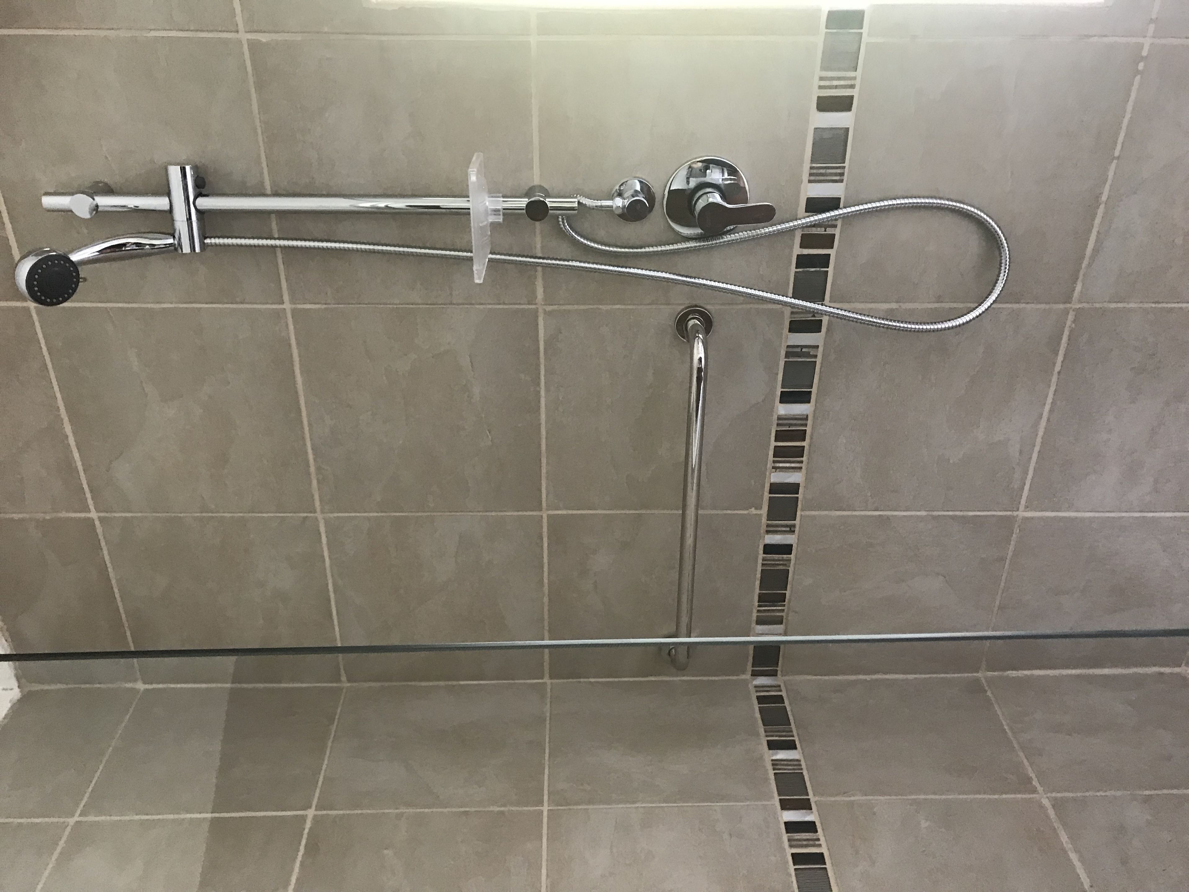 A shower with a handheld showerhead and a fixed showerhead, both mounted on a tiled wall.