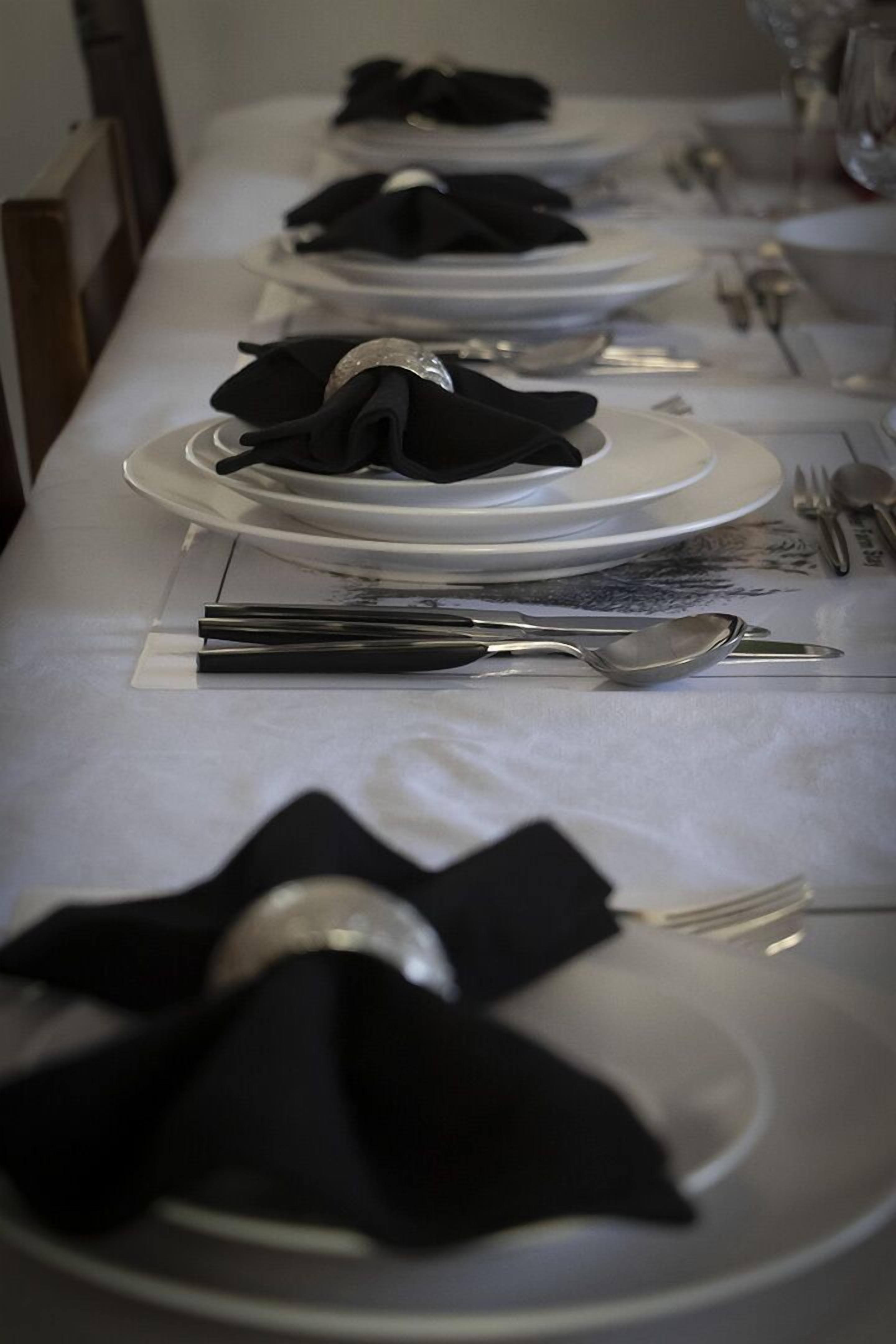 A long table set with white plates, black napkins, and silverware.