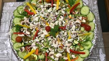 A large, round, foil-covered salad with various vegetables and feta cheese.