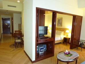 A hotel room with a wooden floor, a bed with white linens, a television, a bedside table with a lamp, and a small table with a tissue box. - Go Daily service (Kuala Lumpur)