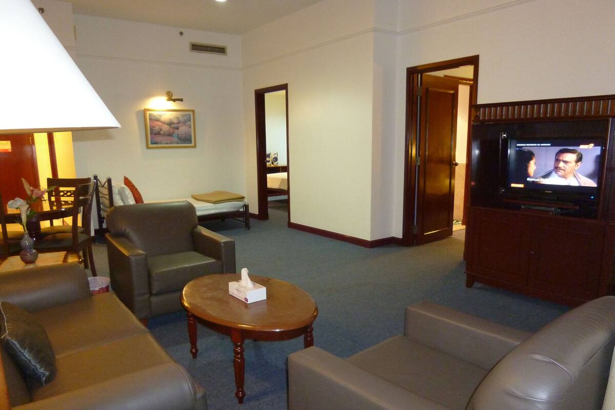 A hotel room with a TV, leather sofas, a small table, and a bed.