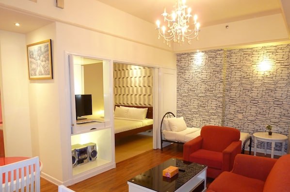 A compact living space with a bed, a television, a red armchair, a small table, and a chandelier. - Go Daily service (Kuala Lumpur)