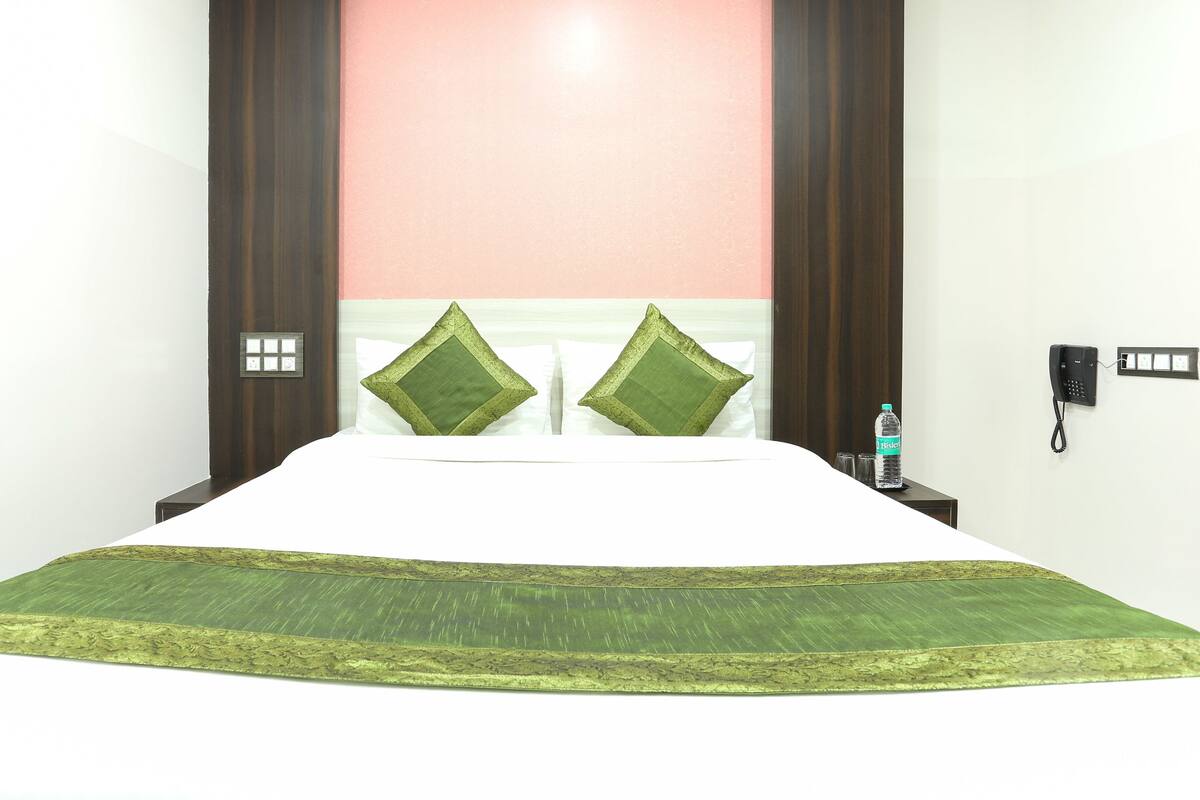A hotel room with a bed, two pillows, a nightstand, a water bottle, and a phone on the wall.