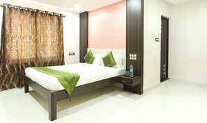 A modern hotel room with a bed, a nightstand, a water bottle, and a door. - Treebo Habitat Suites and Rooms (Bengaluru)