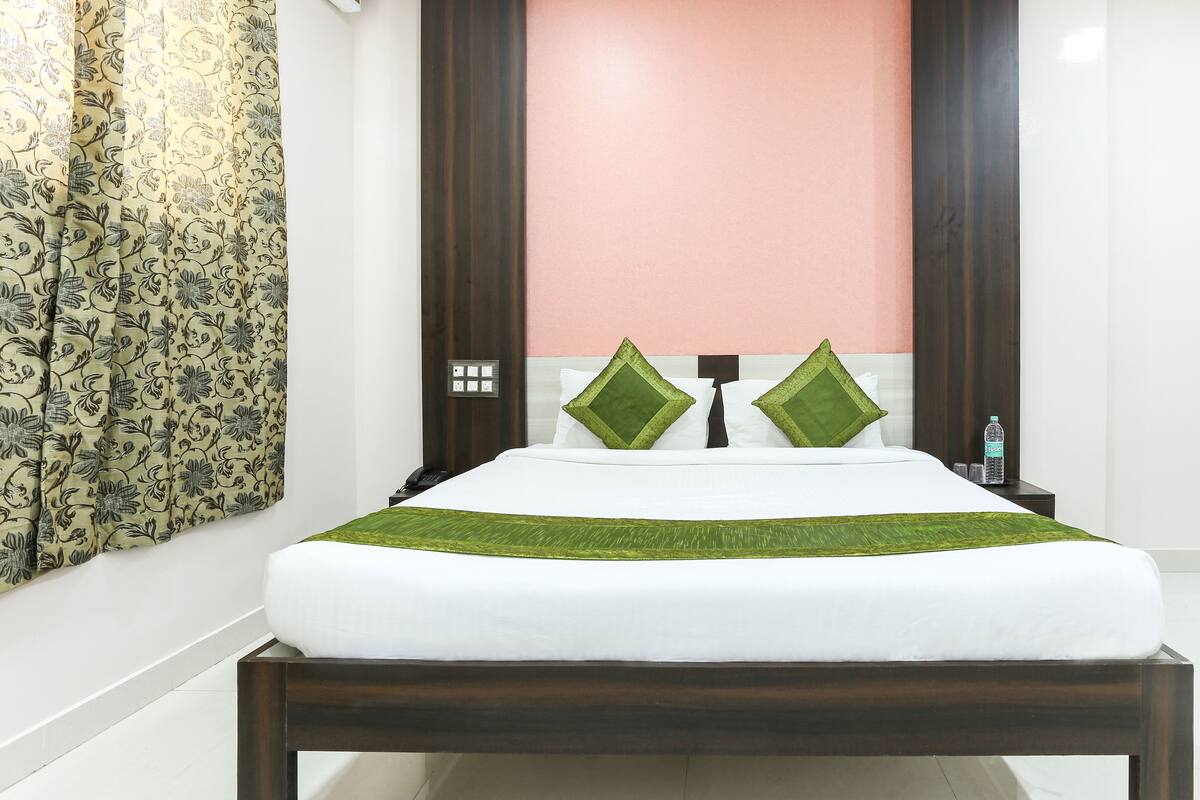 A neatly made bed with a white mattress and green bedspread, a wooden headboard, and two green pillows.