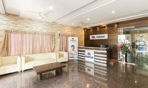 A hotel reception area with a reception desk, a seating area with a sofa and a coffee table, and a stone wall. - Treebo Habitat Suites and Rooms (Bengaluru)
