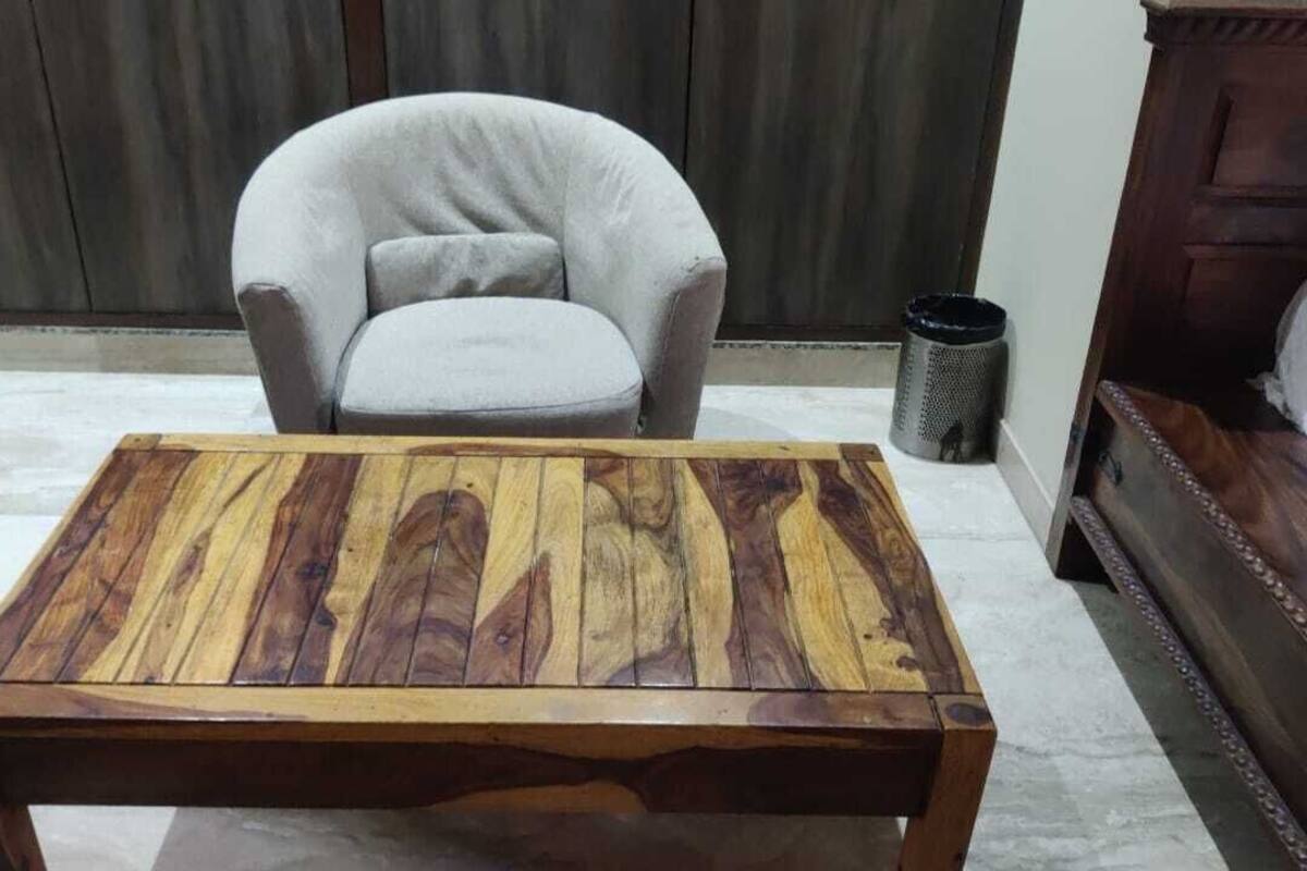 A wooden coffee table with a natural wood grain pattern in a room with a grey armchair and a wooden bed.