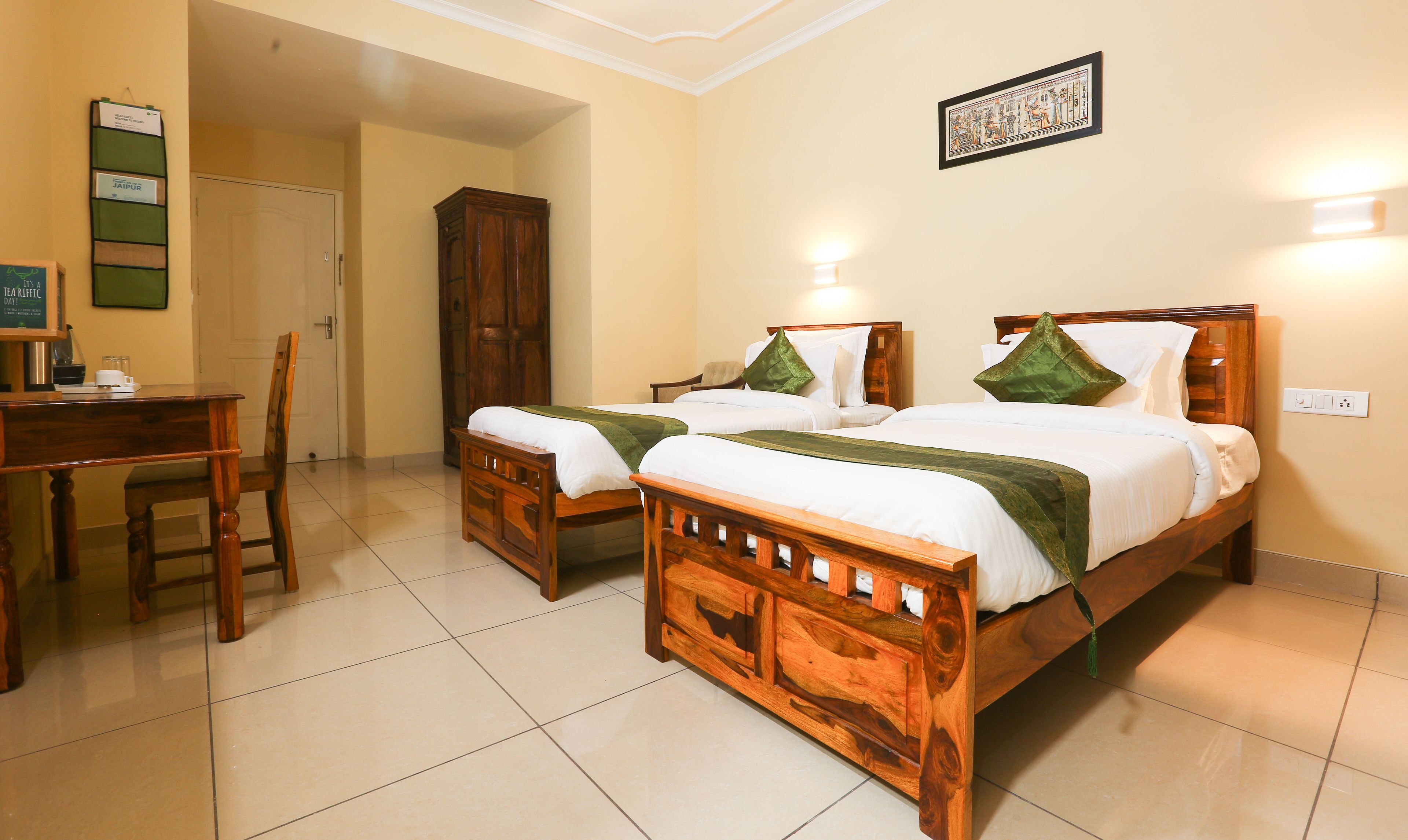 A hotel room with two wooden beds, a desk, a chair, and a cabinet.
