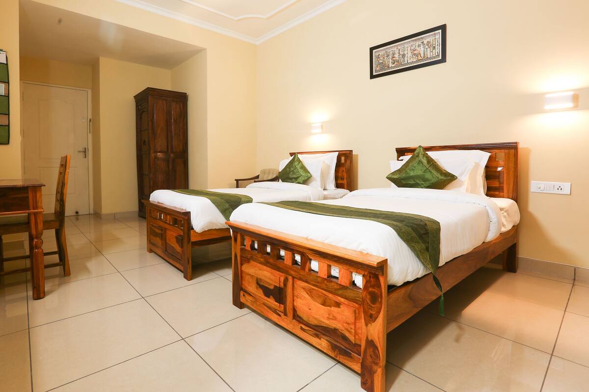 A hotel room with two wooden beds, a desk, a chair, and a cabinet.