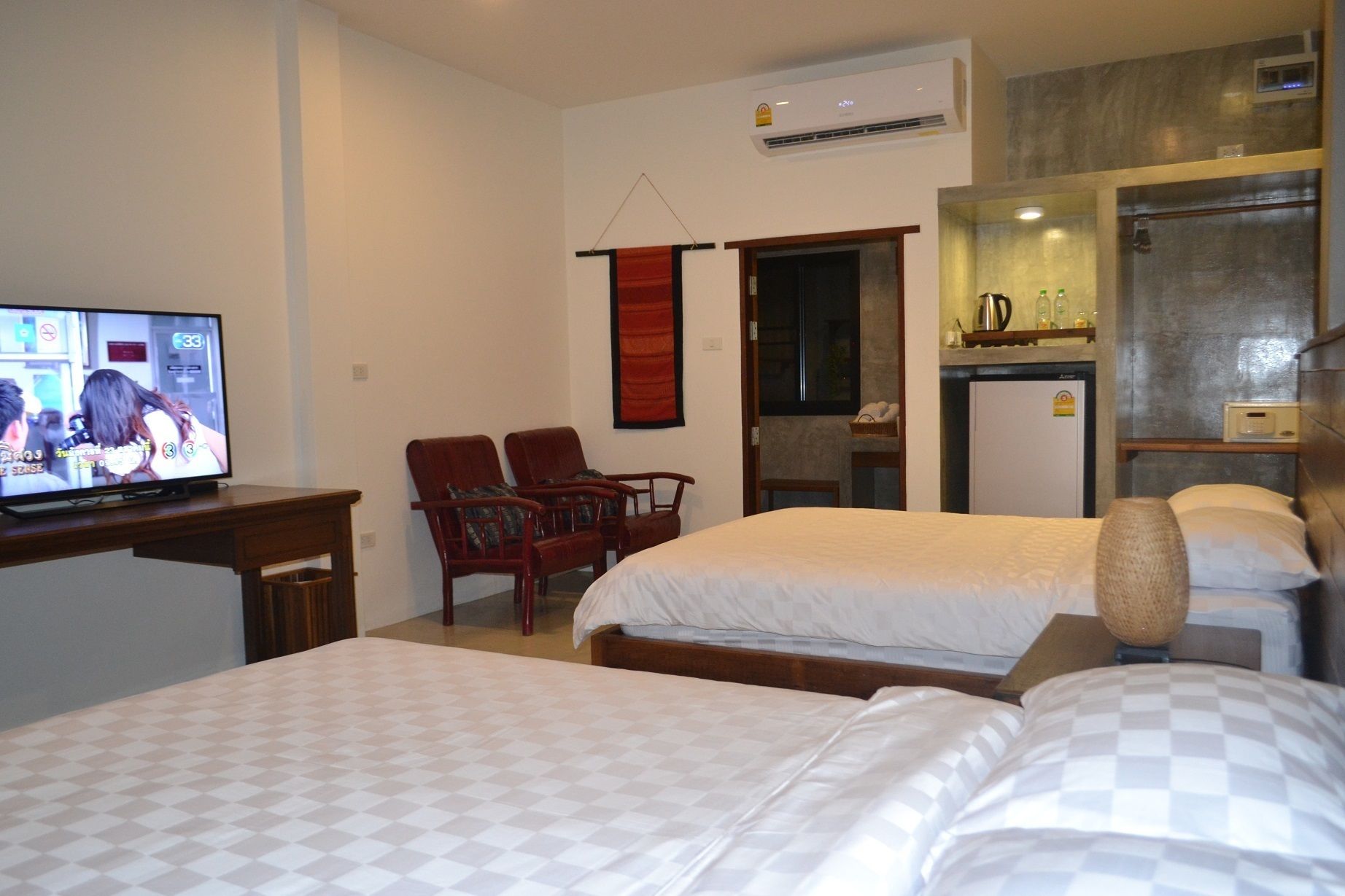 A hotel room with two beds, a TV, a desk, a chair, a small kitchenette, and a red curtain.