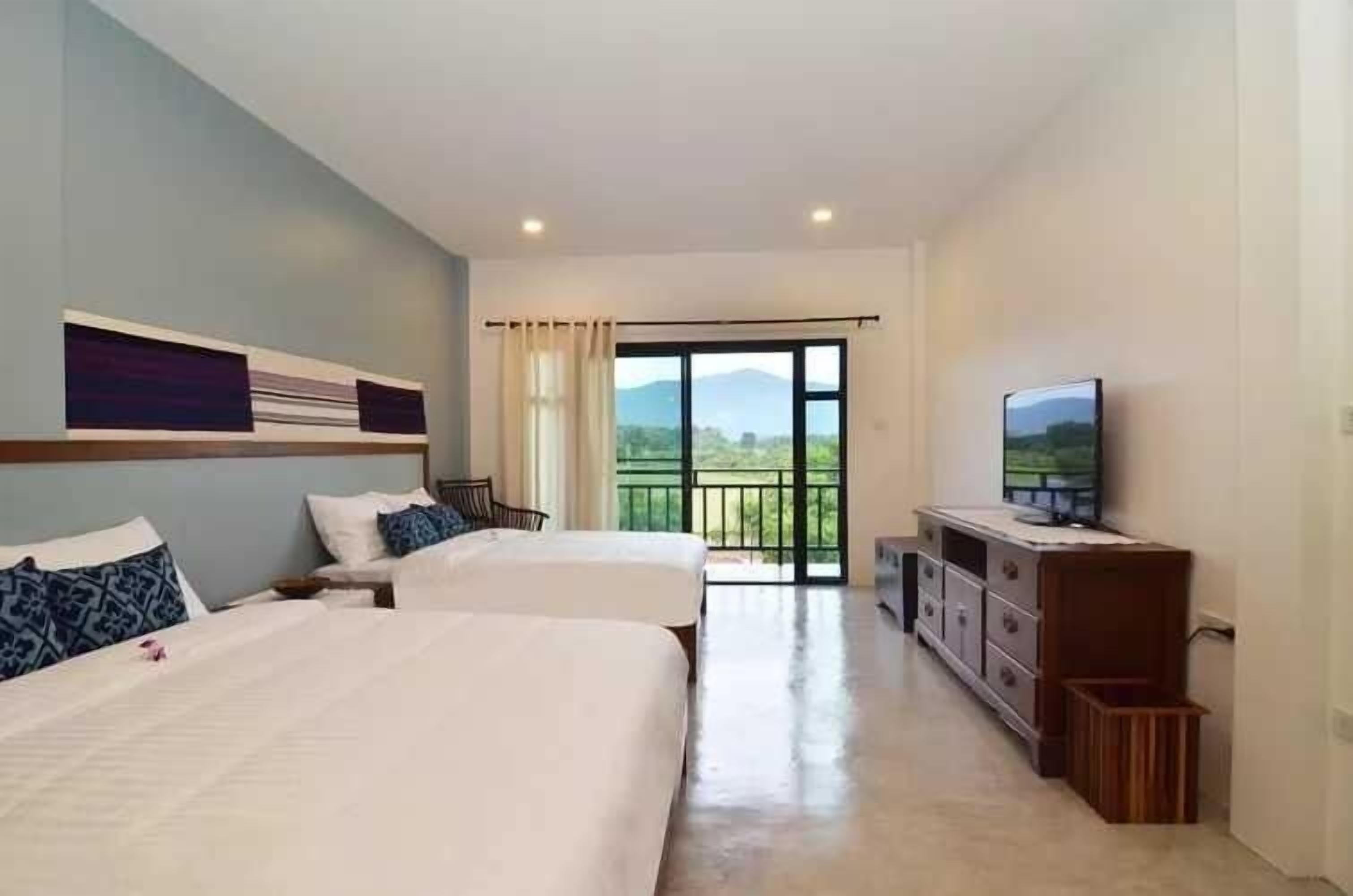 Habitación de hotel con dos camas, televisión y balcón con vistas.