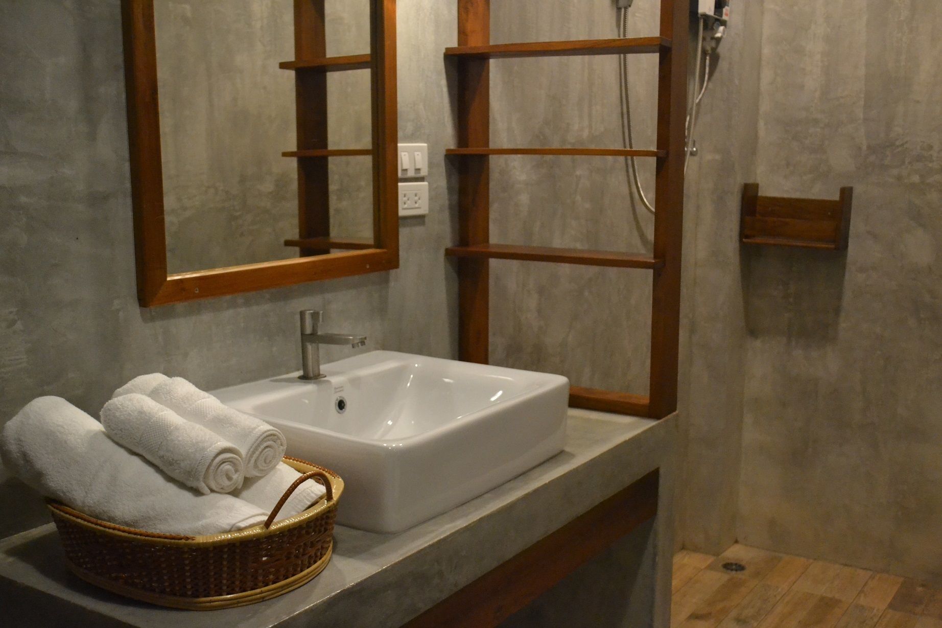 A bathroom with a white sink, a wooden-framed mirror, a shower, and a wicker basket with towels.