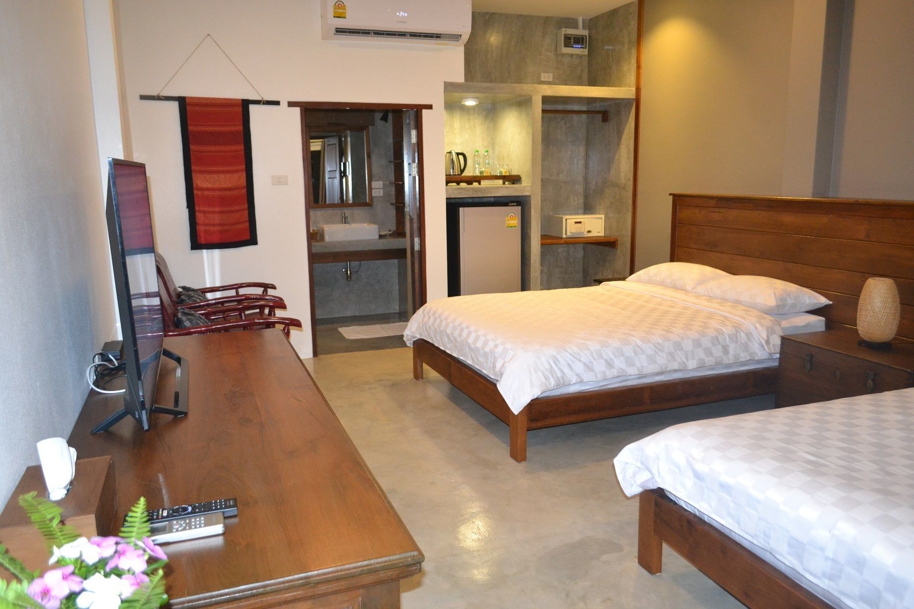 Een hotelkamer met een houten bed, een bureau met stoel, een televisie en een kleine kitchenette.