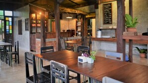 A rustic cafe with wooden tables and chairs, a chalkboard menu, and potted plants. - Le Cocotier Resort (Mae Taeng)