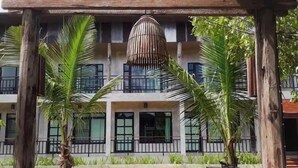 A building with a central entrance, surrounded by palm trees and a wooden pergola. - Le Cocotier Resort (Mae Taeng)