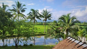 A tropical landscape with palm trees, a pond, and a thatched structure. - Le Cocotier Resort (Mae Taeng)