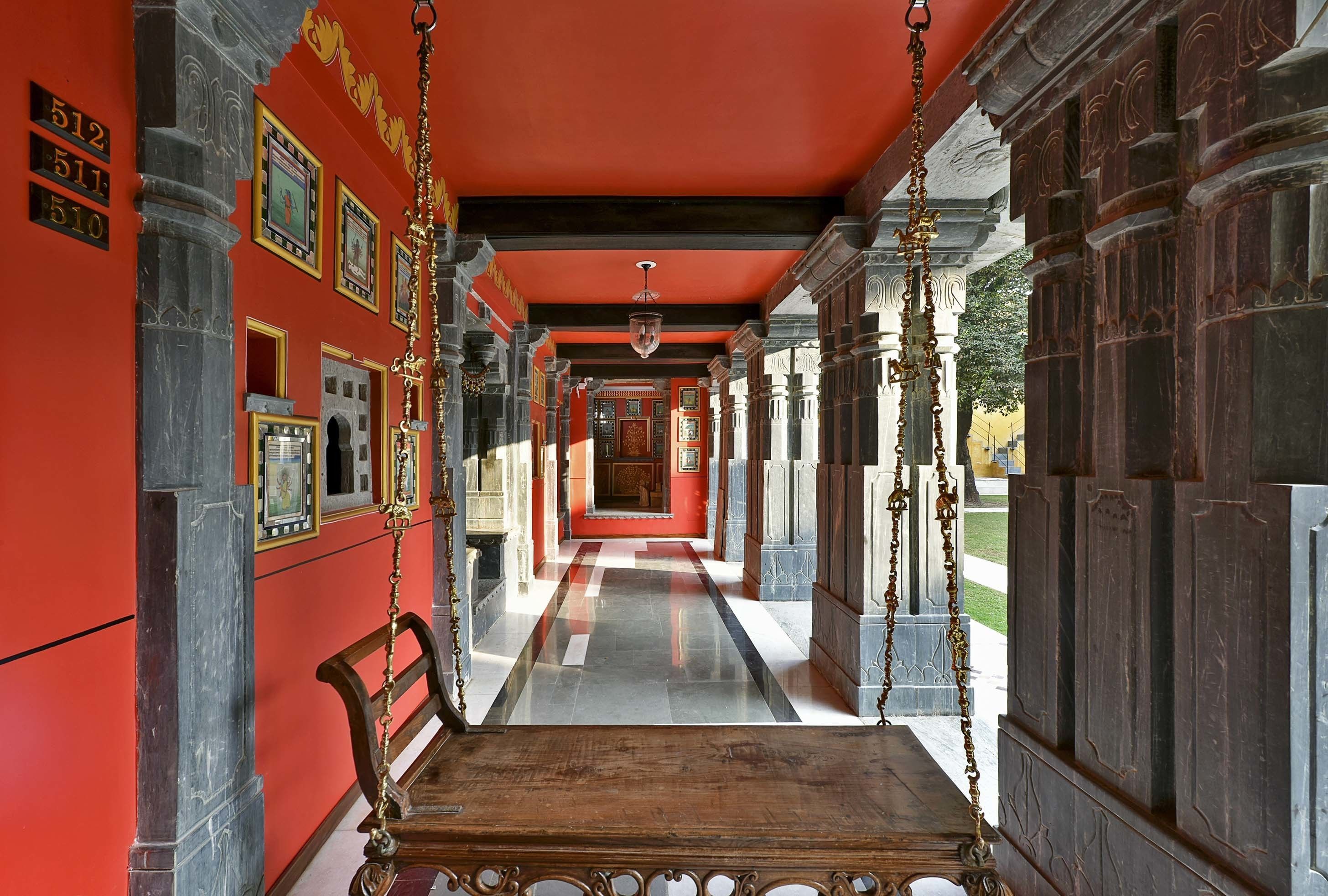 A corridor with a red wall, numbered plaques, and a wooden bench.