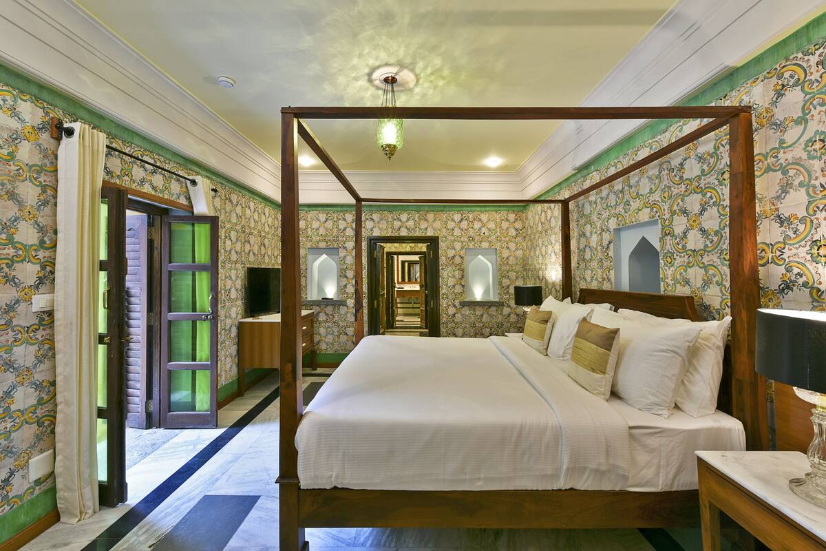 A four-poster bed with a canopy, a wooden nightstand, a bedside table with a lamp, and a mirror on the wall.