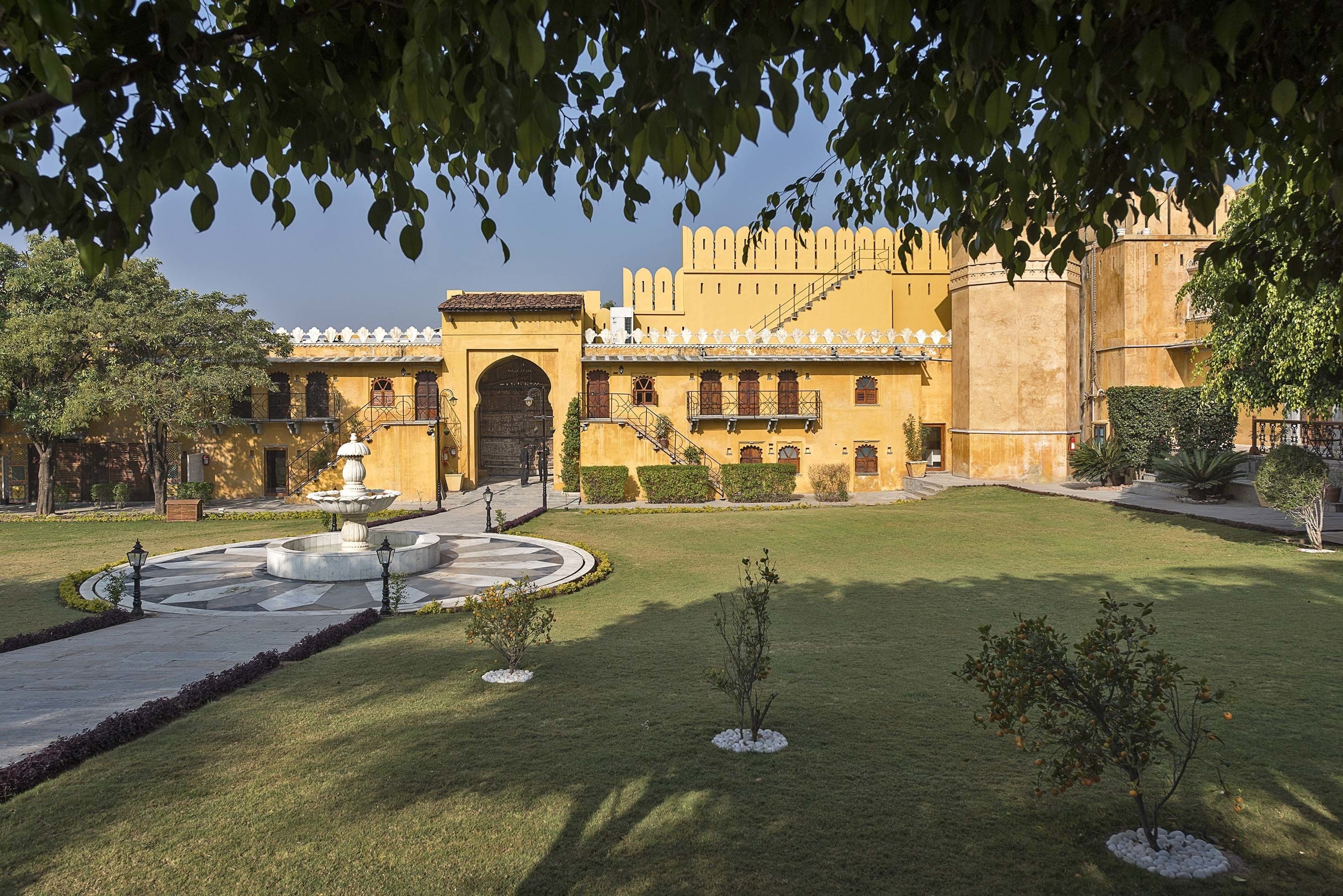 A courtyard with a fountain, a large building with a yellow facade, and a clear sky.