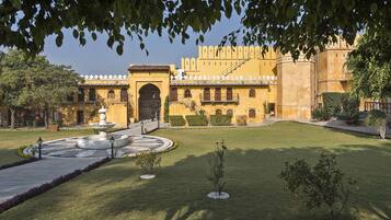 A courtyard with a fountain, a large building with a yellow facade, and a clear sky.