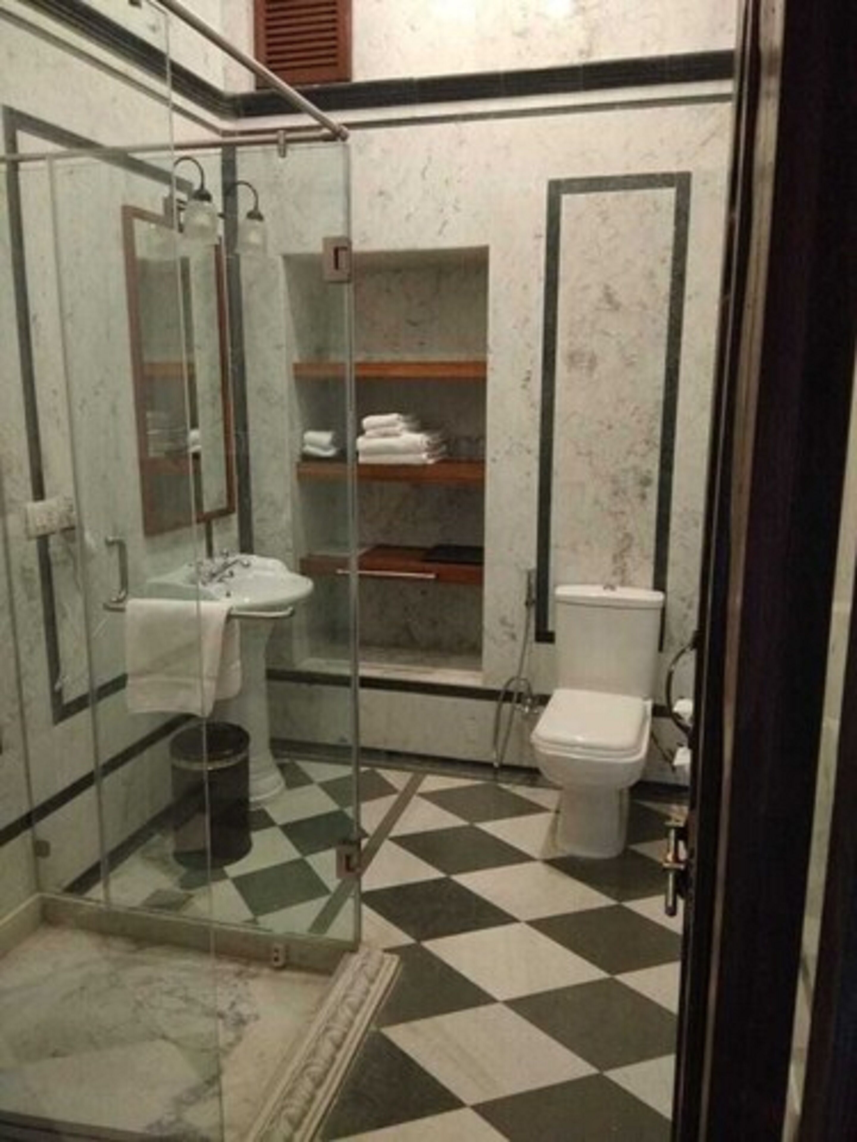 Ein Badezimmer mit einer gläsernen Duschkabine, einem Waschbecken, einer Toilette und einem Regal mit gefalteten Handtüchern.