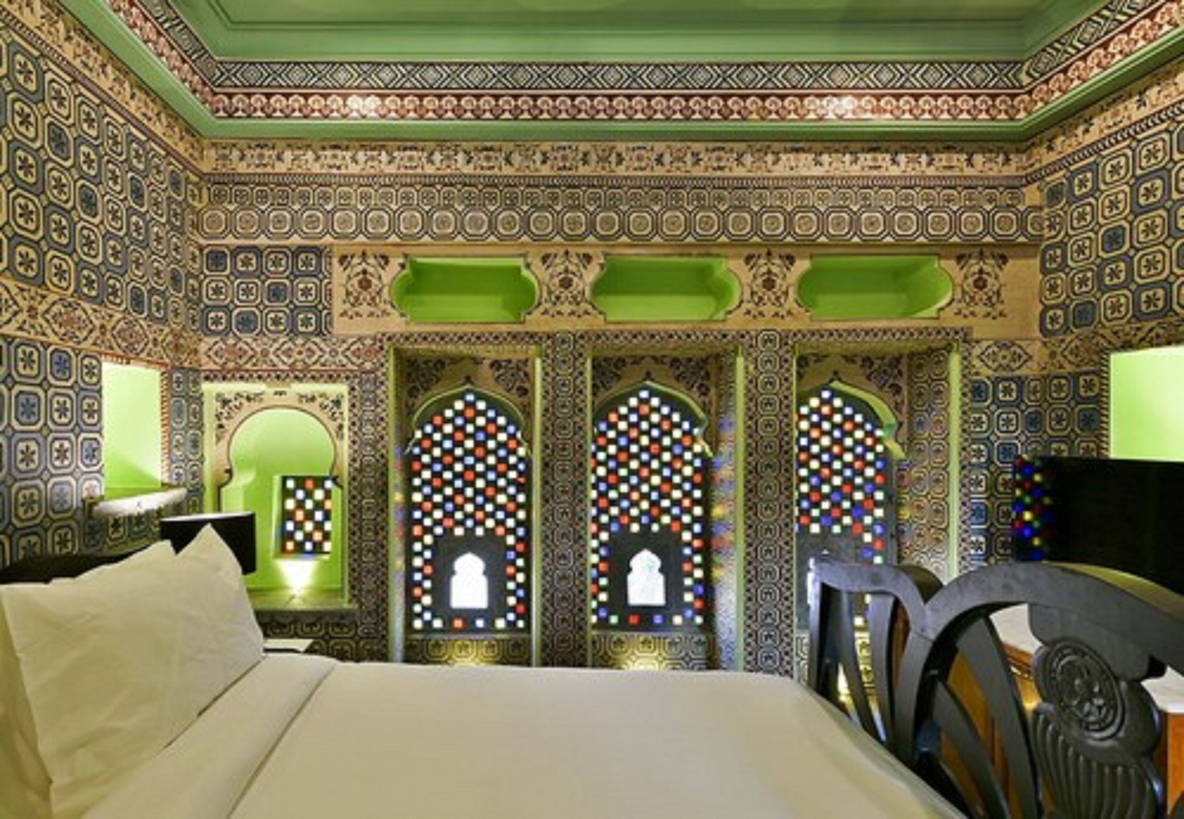 A room with patterned walls, a bed, and arched windows with colorful lights.
