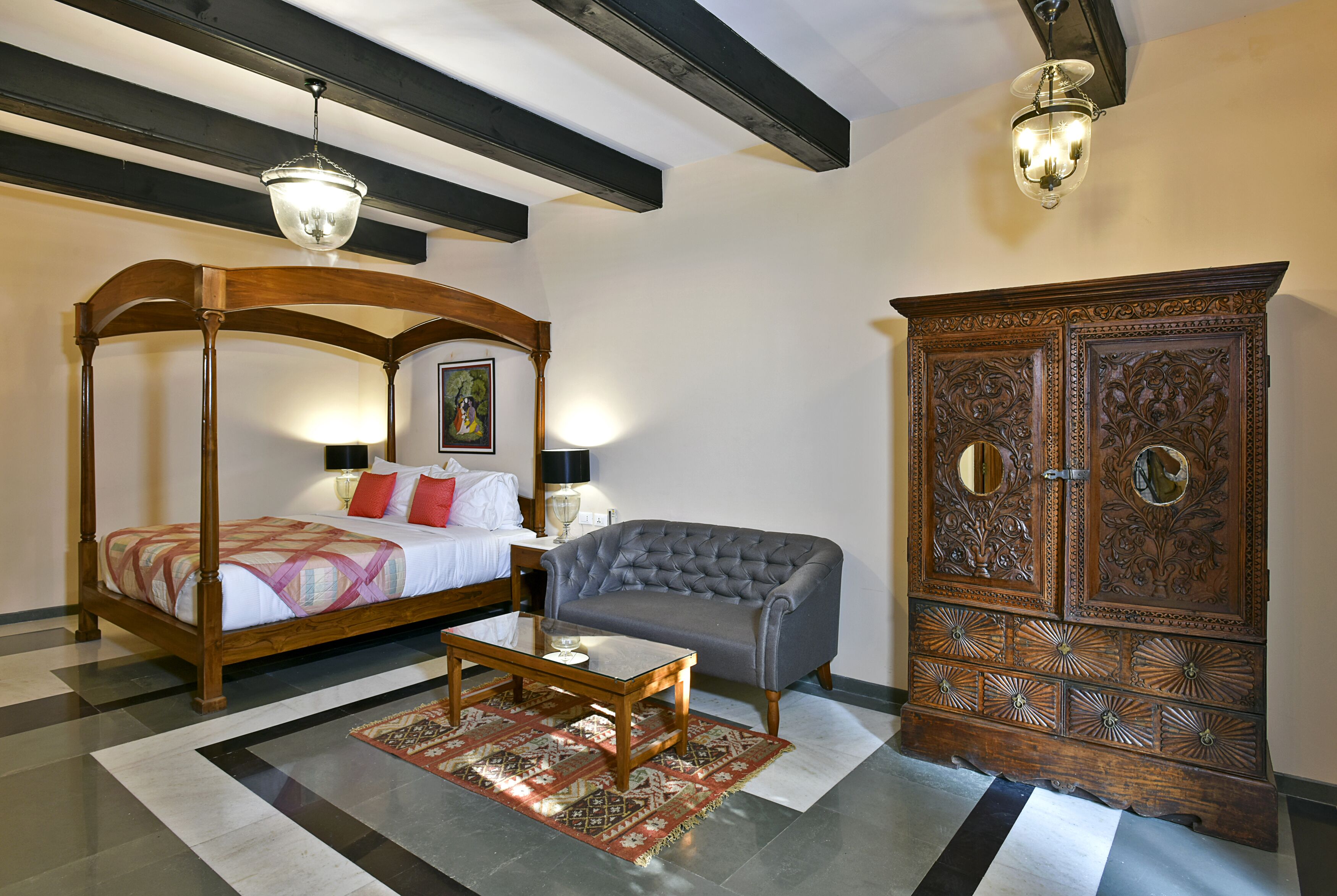 A bedroom with a four-poster bed, a grey sofa, a wooden cabinet, and a patterned rug.