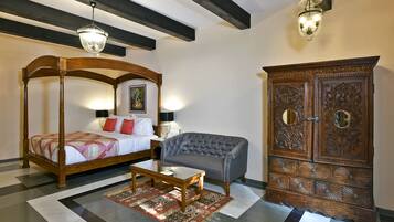 A bedroom with a four-poster bed, a grey sofa, a wooden cabinet, and a patterned rug.