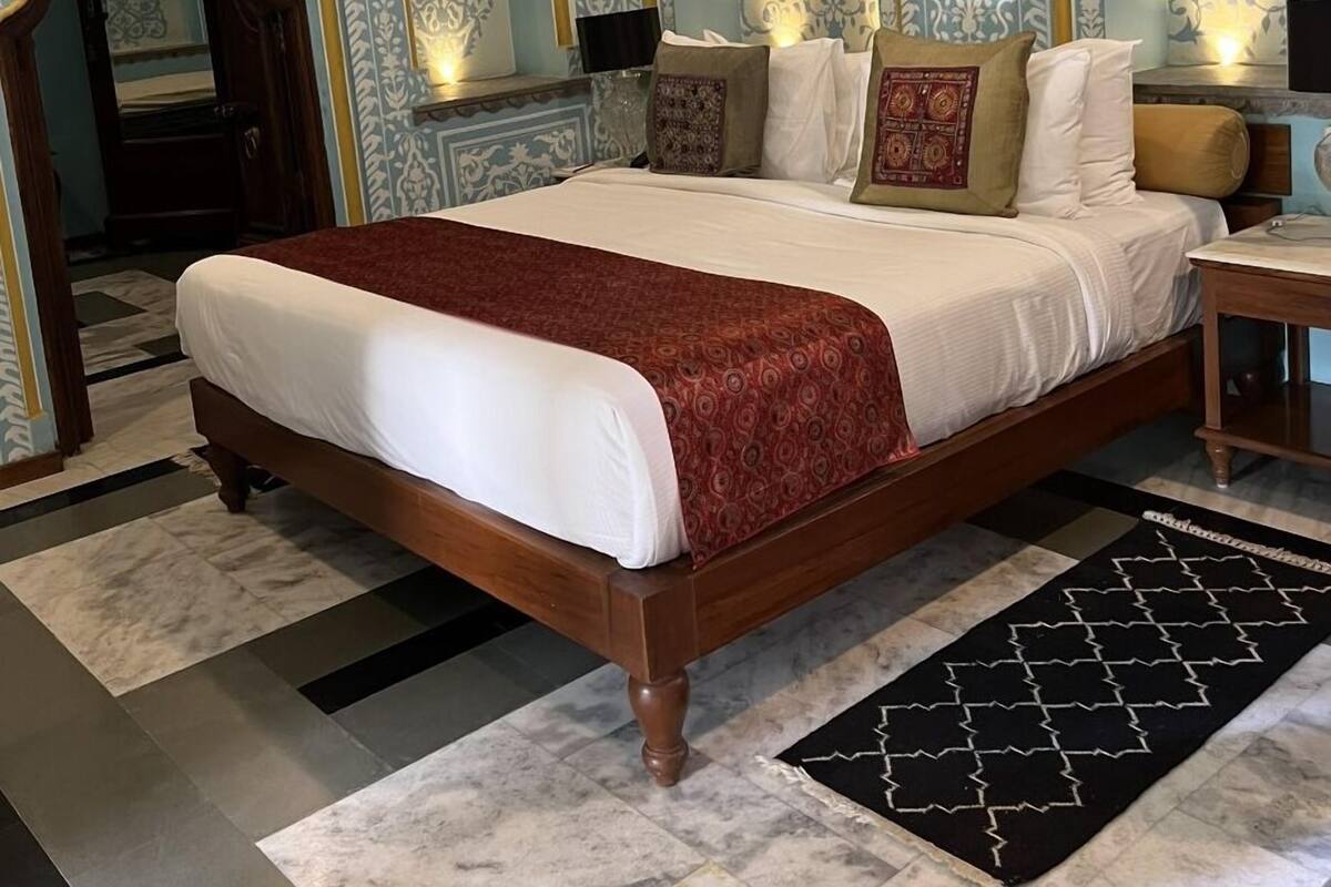 A spacious bedroom with a large bed, ornate wall designs, and a classic wooden floor.