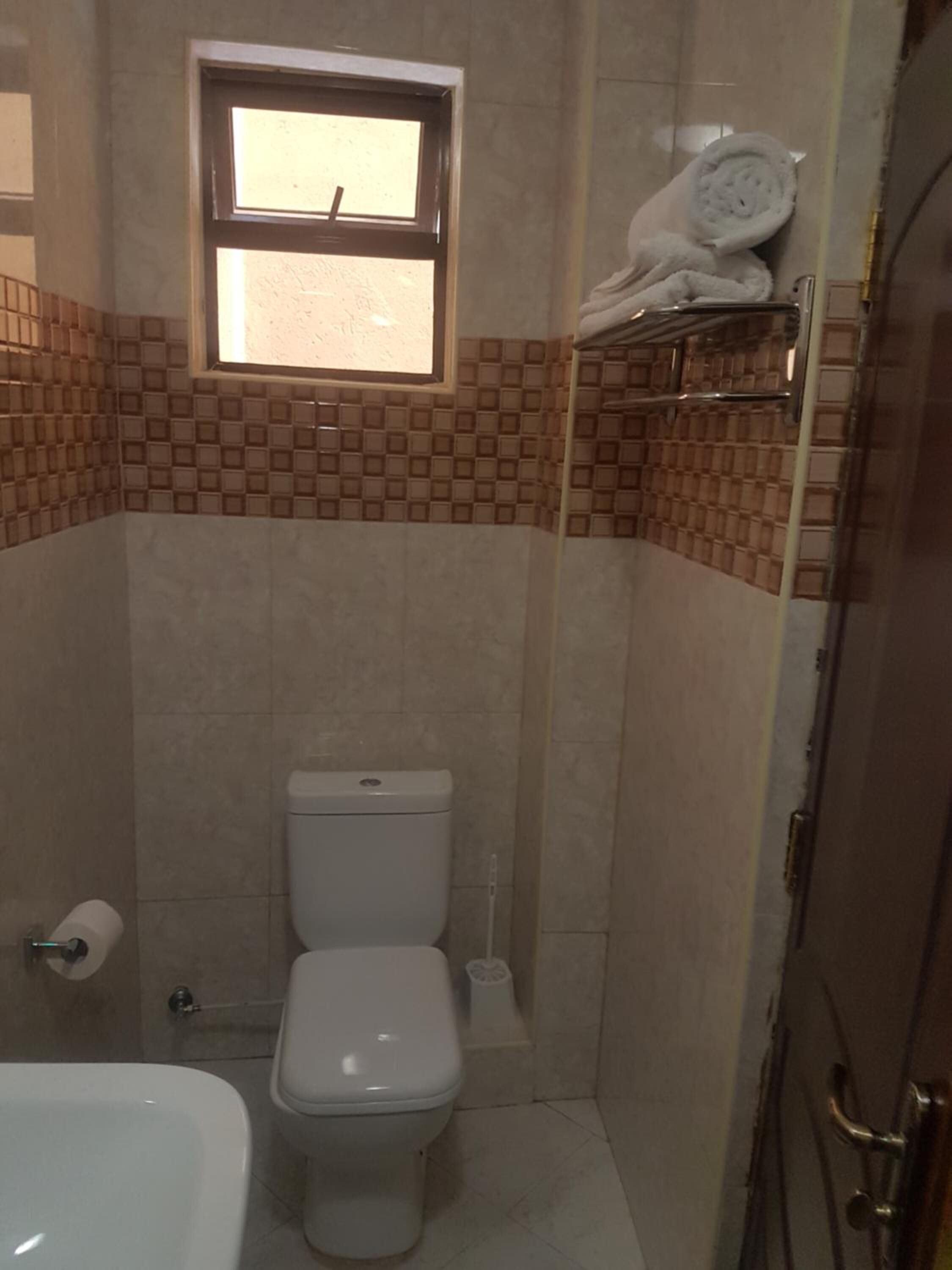 Een badkamer met toilet, een klein raam en een handdoekhouder.