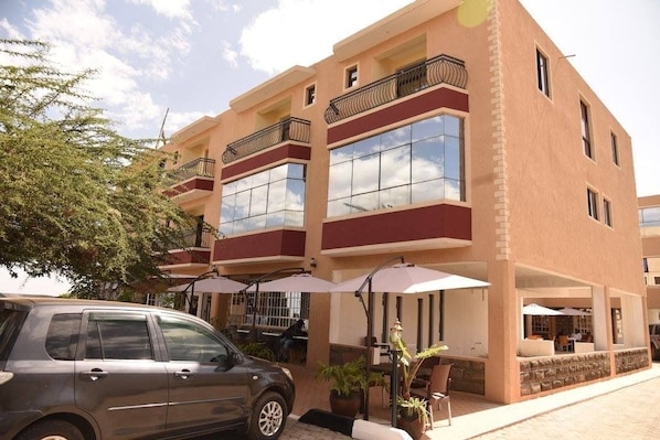 A multi-story hotel with balconies, outdoor seating, and a car parked in front.