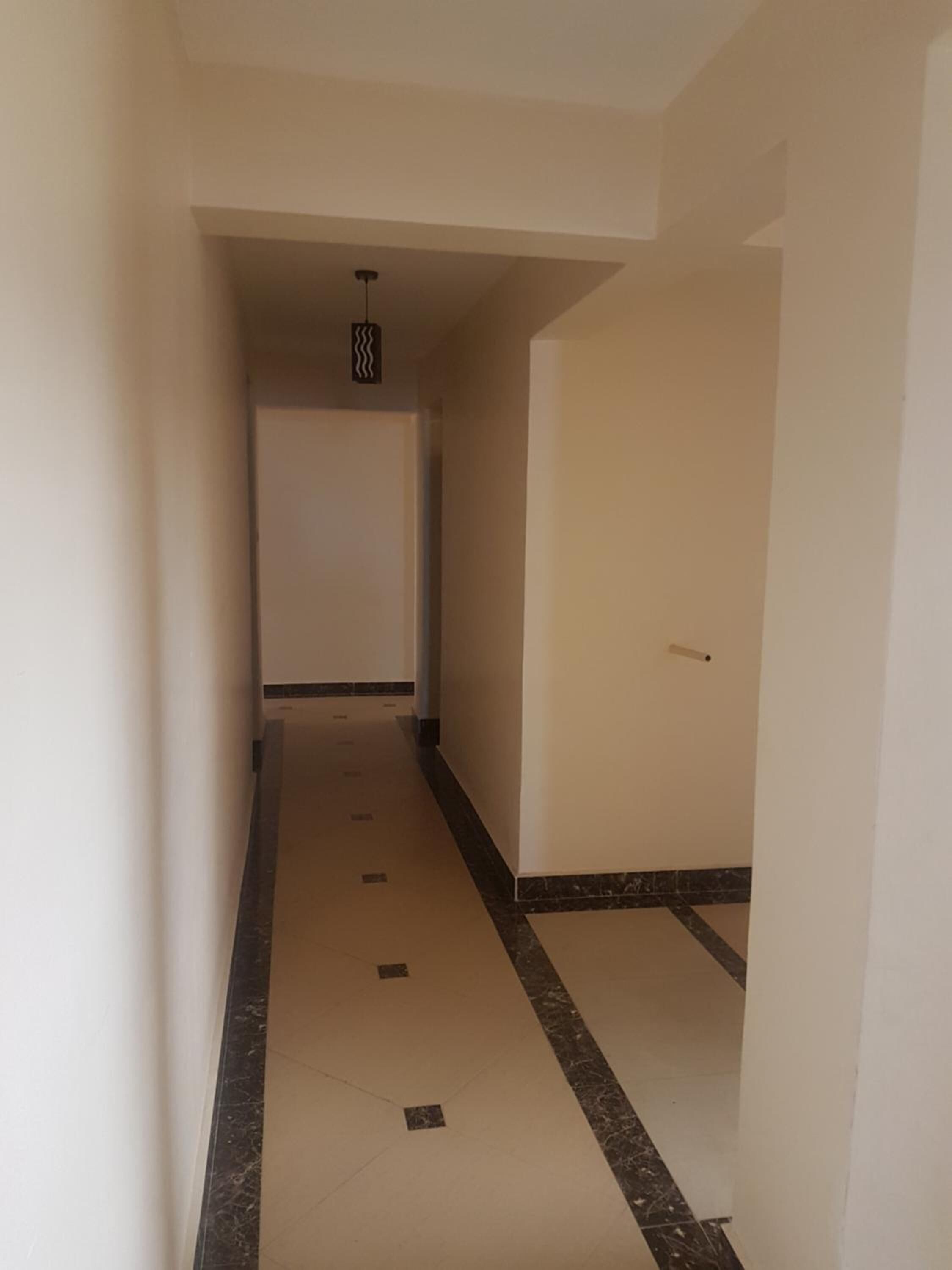 Un corridoio stretto con pavimento piastrellato, pareti bianche e una lampada a soffitto.