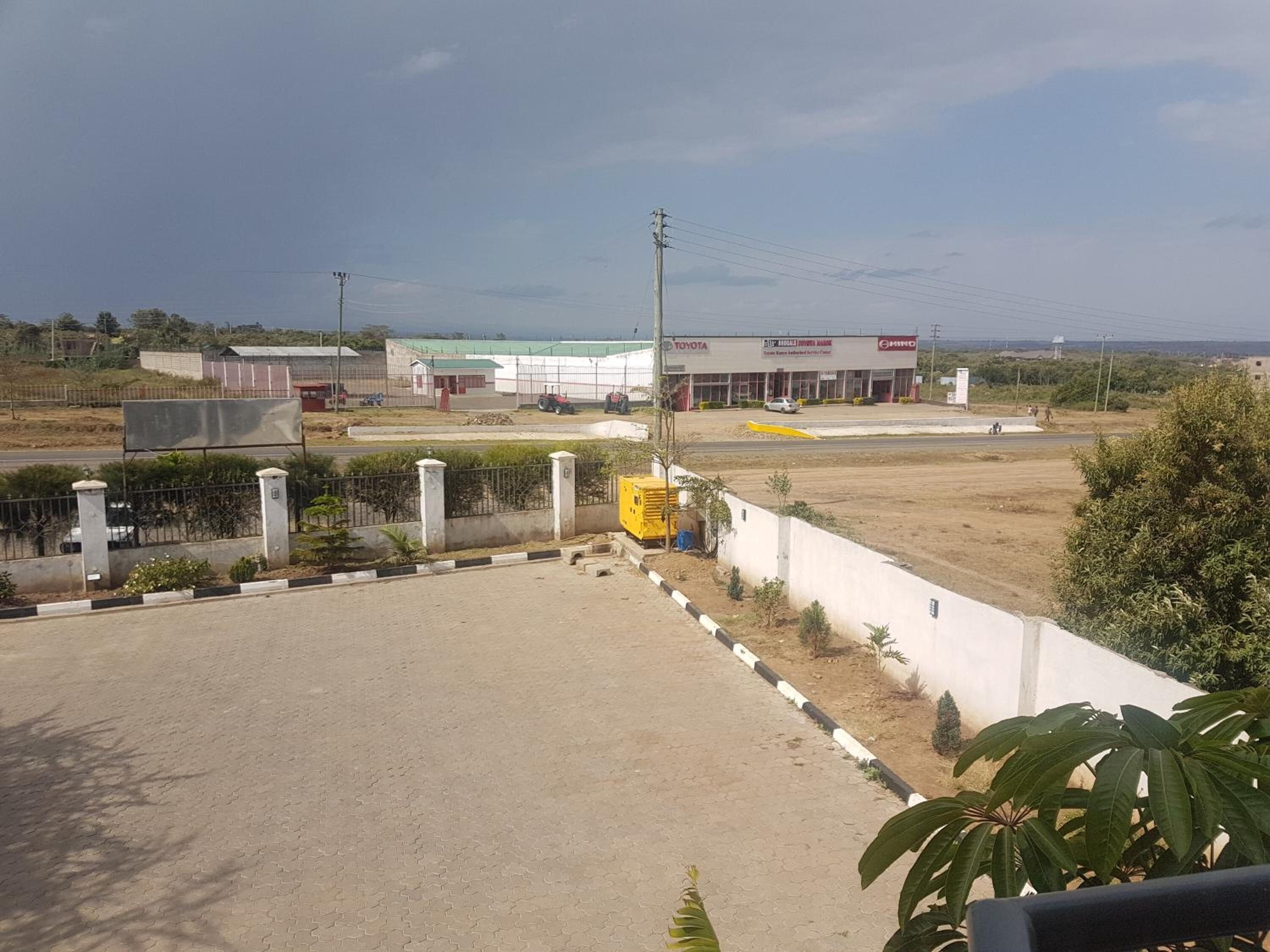 Un estacionamiento vacío con un camino pavimentado, un contenedor amarillo y una valla.