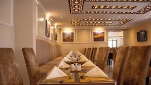 A dining area with a long table set for a meal, surrounded by cushioned booths, and framed artwork on the walls. - Mara Frontier Hotel (Narok)