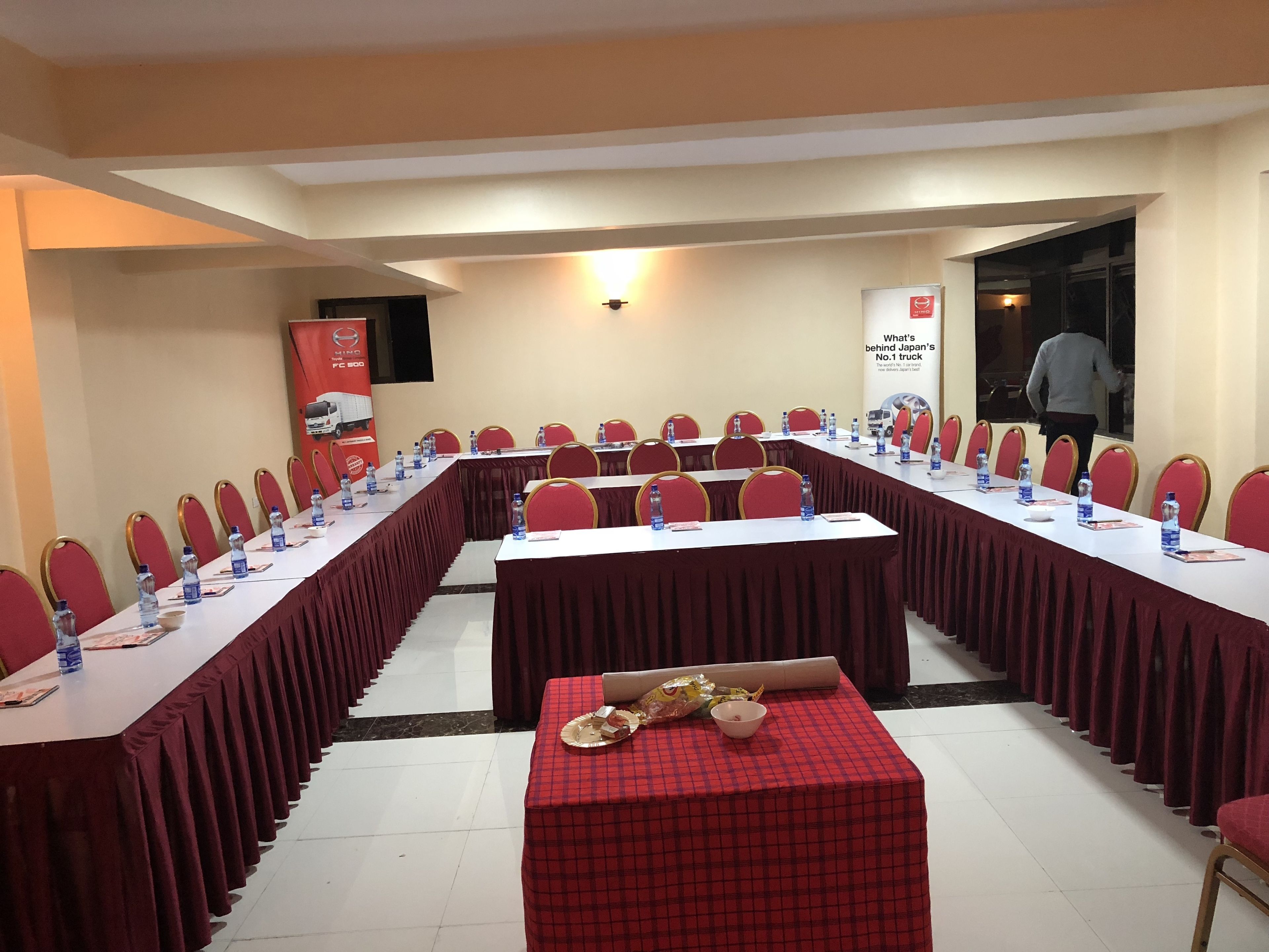 A conference room with long tables, red chairs, and water bottles.