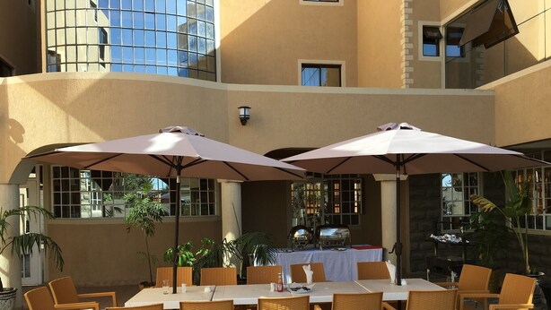 An outdoor patio with a table set for dining, surrounded by wicker chairs and large umbrellas. - Mara Frontier Hotel (Narok)