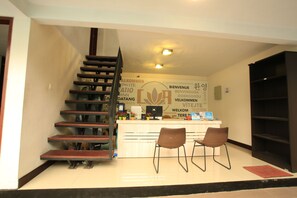 A reception area with a staircase, a reception desk, two chairs, and a wall with multilingual welcome signs.